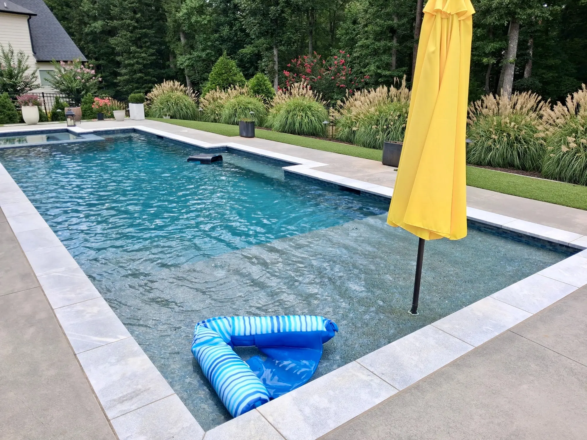 Family pool with a sun shelf, garden border, and yellow umbrella