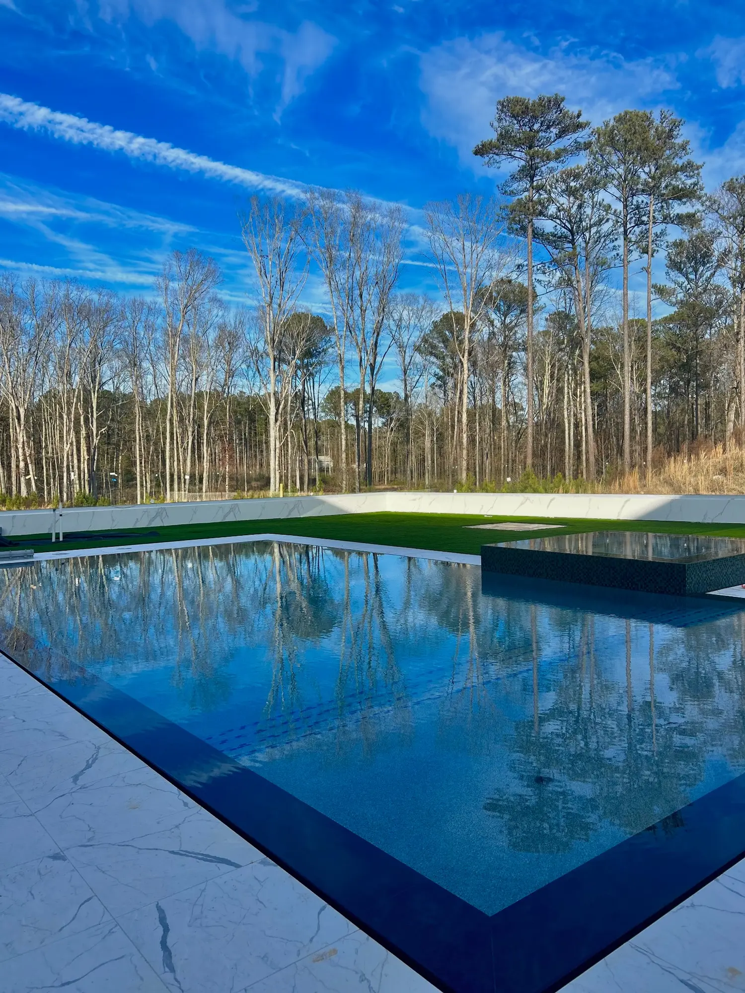 Modern geometric pool reflecting the blue sky and surrounding trees