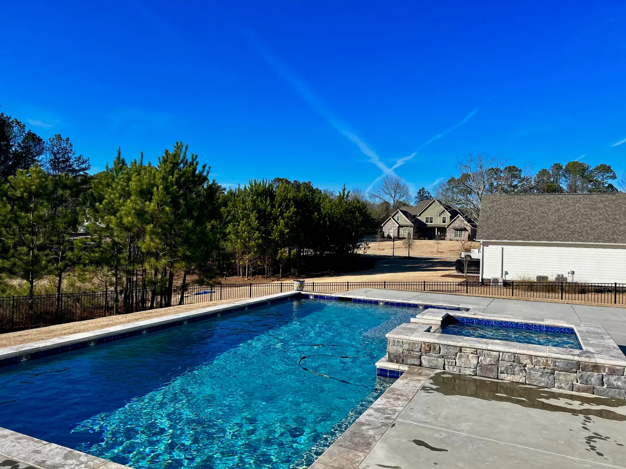 Bright blue pool with a raised stone spa and wooded backdrop