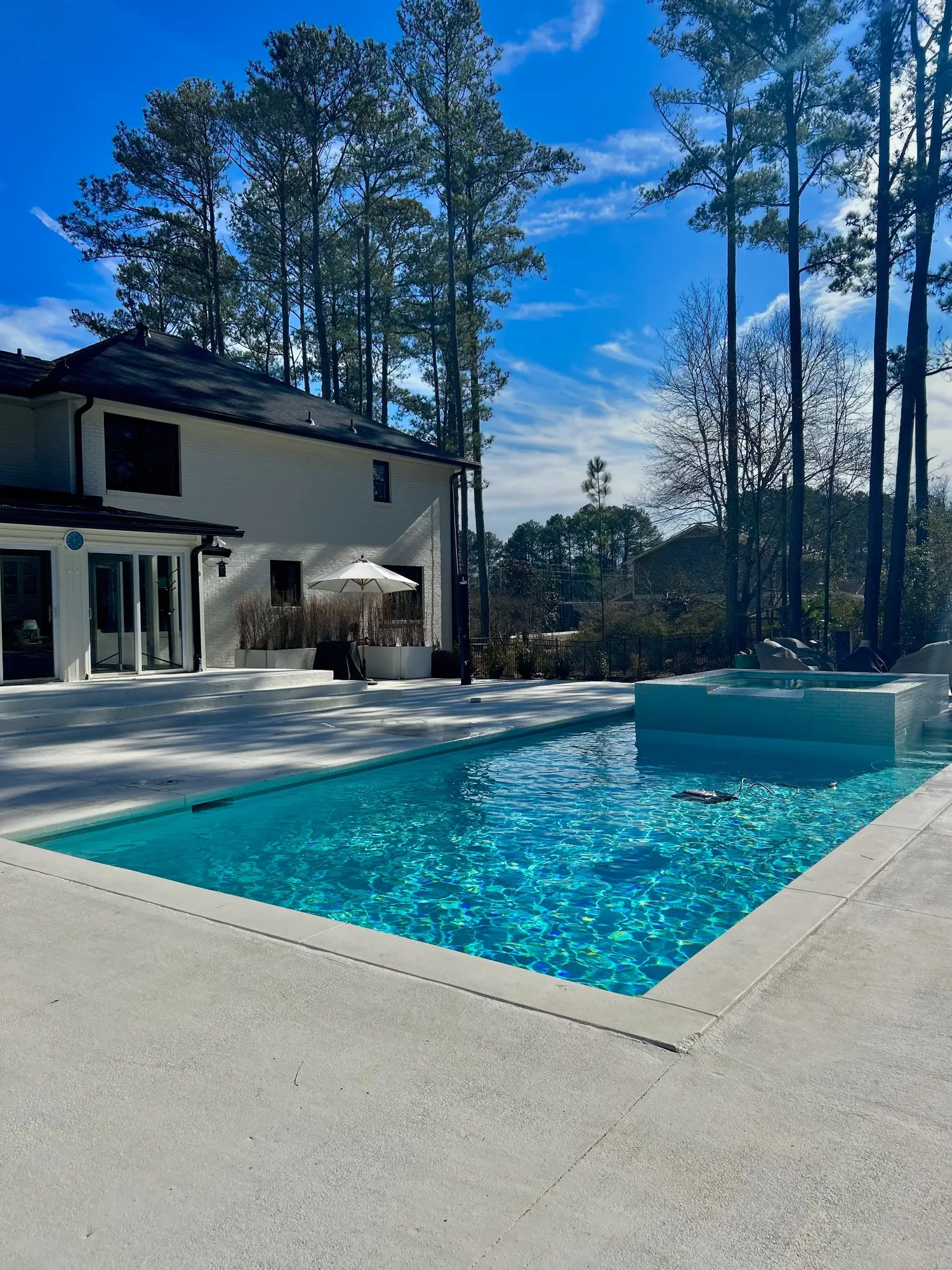 Clear pool and raised spa beside a white home
